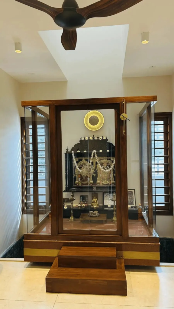 Elegant custom pooja room design with traditional brass elements and modern glass display case by Elegante Interiors Bangalore
