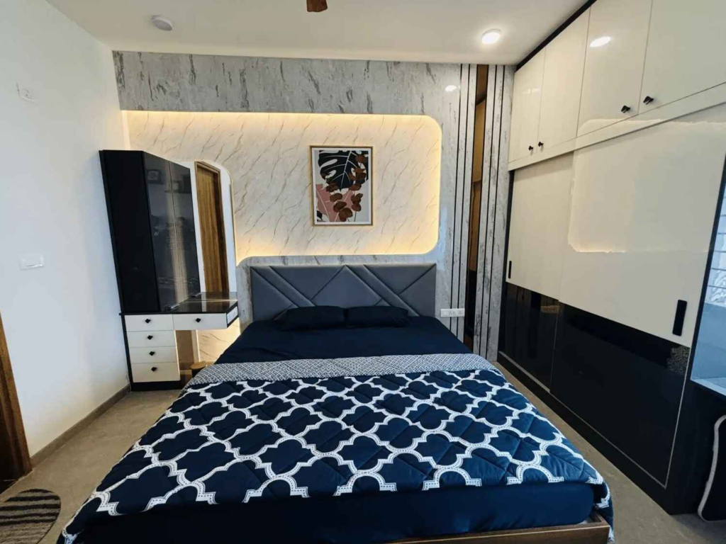 Modern bedroom design with warm backlit wall panel, elegant wardrobe, and cozy navy bedding by Elegante Interiors Bangalore