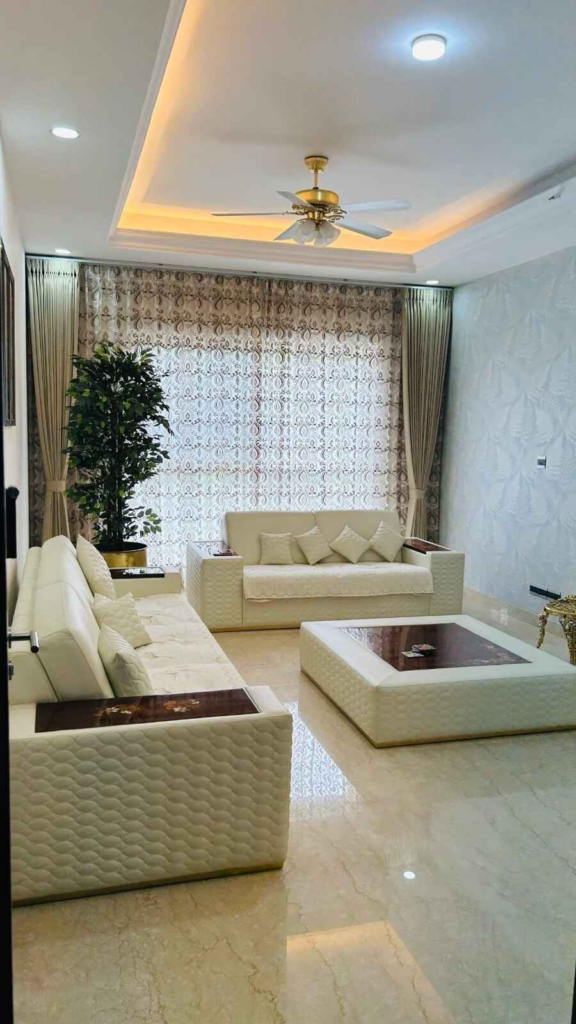 Sophisticated living room interior by Elegante Interiors featuring cream quilted furniture, decorative wallpaper accent wall, and warm ambient lighting in Bangalore home