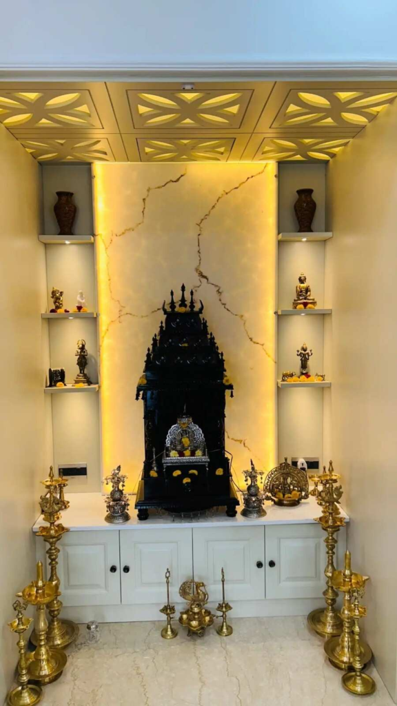 Traditional pooja room interior design by Elegante Interiors featuring decorative ceiling work, marble backdrop, integrated lighting, and brass traditional elements